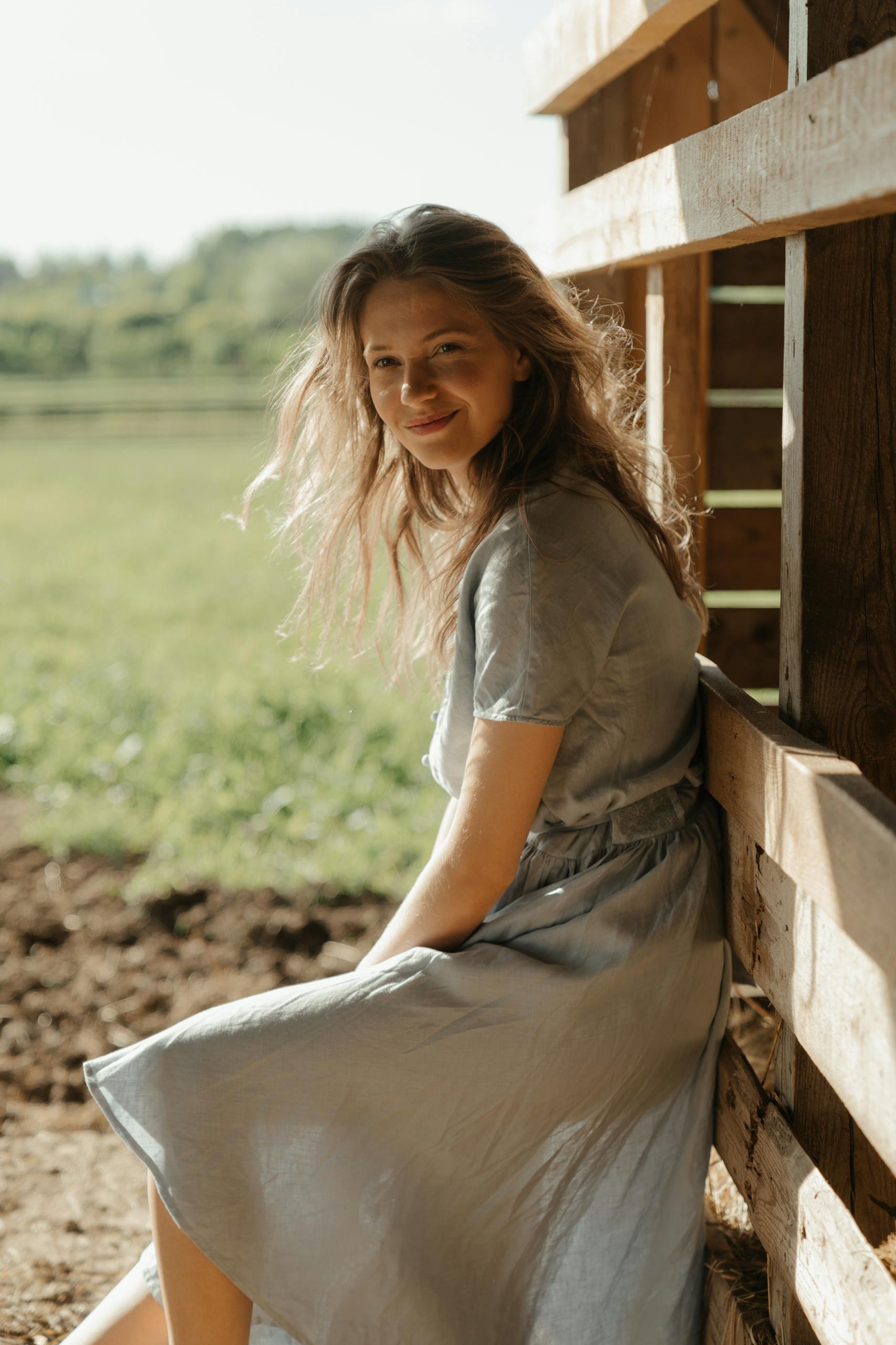 A young woman in a dress enjoying a serene moment outdoors by a farm building.
